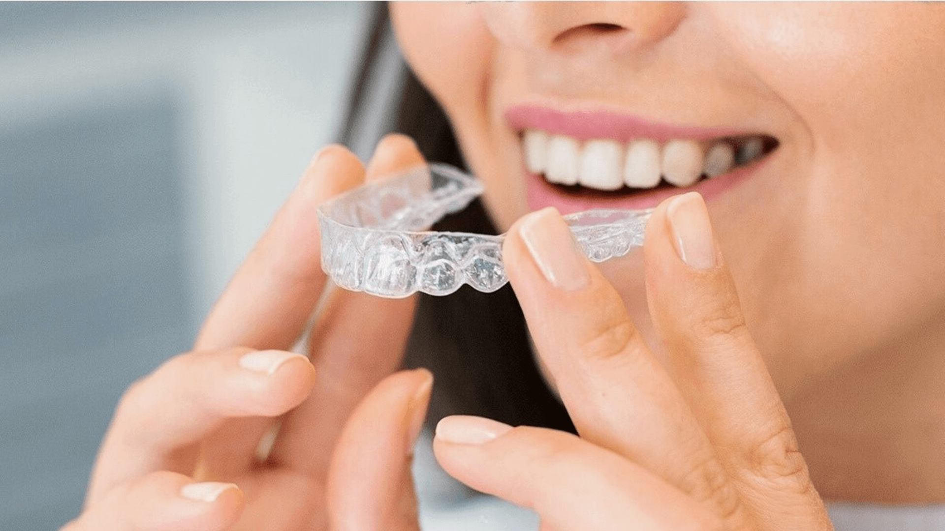 Close-up de una paciente adulta poniéndose un alineador dental transparente (Invisalign) con ambas manos. Es la imagen de portada para el post sobre mitos de la ortodoncia invisible en BEJA Dental, Lanzarote.